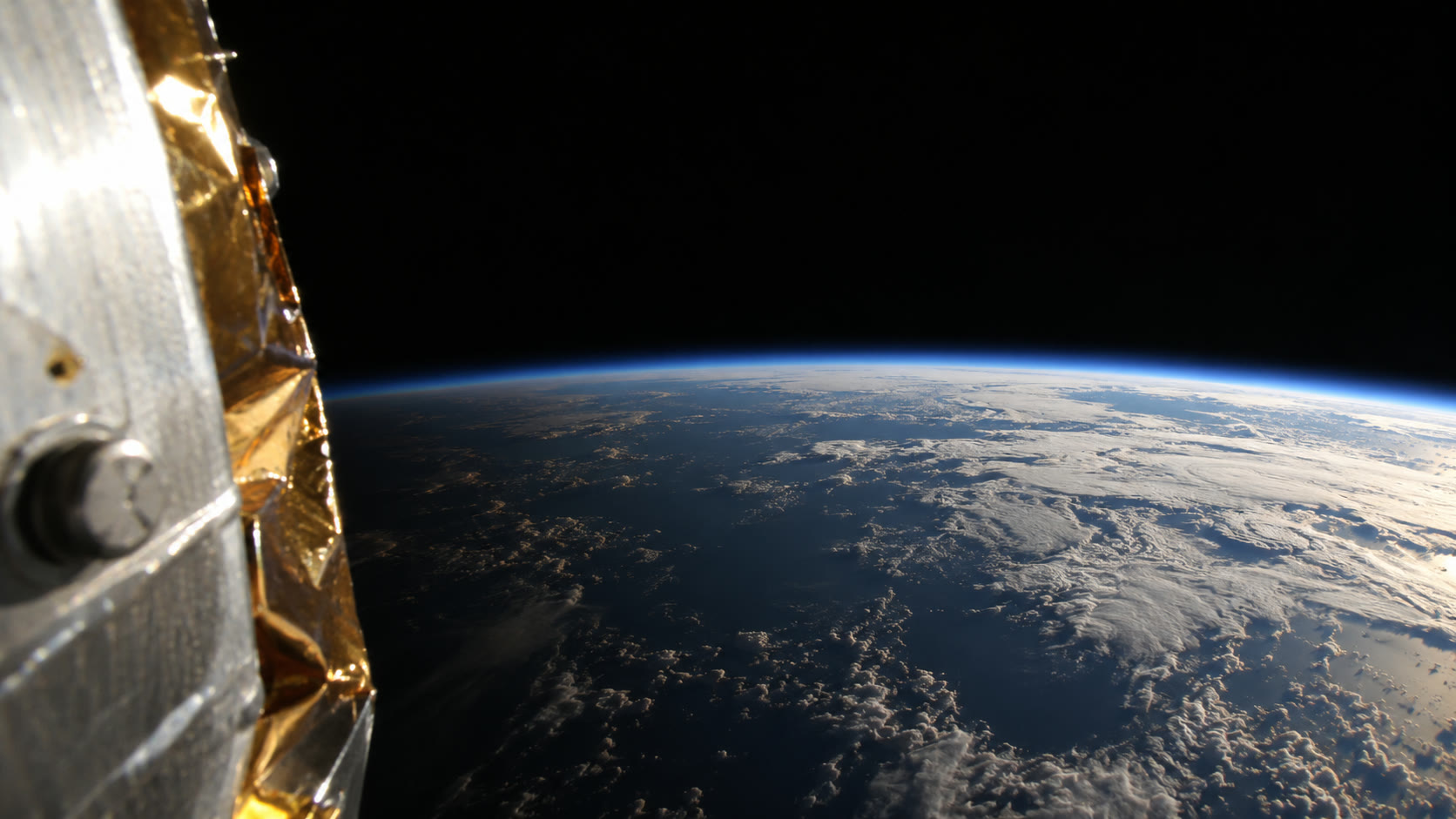 The curve of the Earth and a thin blue line of atmosphere, with the edge of the capsule and gold tape in the foreground.